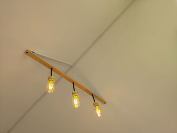 Low angle view of illuminated light bulb hanging on ceiling