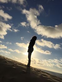 Tilt image of silhouette woman standing at beach against sky during sunset