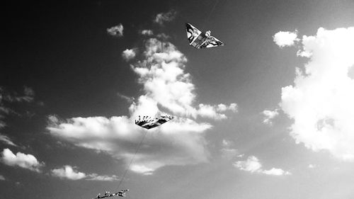 Low angle view of kites flying in cloudy sky