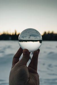 Close-up of hand holding crystal ball against calm lake