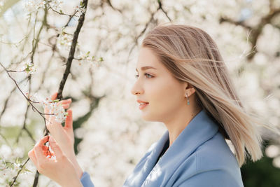 Young beautiful blonde woman in blooming apple garden.