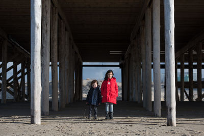 Full length of siblings standing under bridge at beach