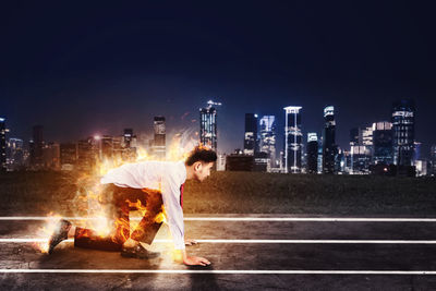 Side view of young man standing against illuminated buildings in city