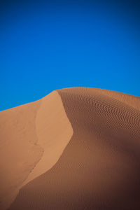 Sand dunes in desert against clear blue sky