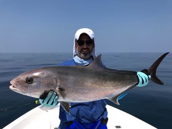 Portrait of smiling man holding fish on boat in sea against clear blue sky