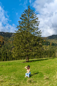 Young woman sitting in the middle of a green pasture in mountains.