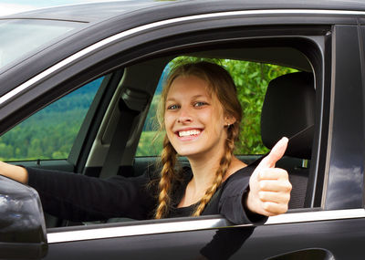 Portrait of smiling young woman showing thumbs up sign in car