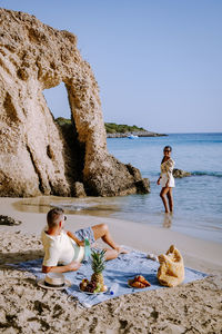 Full length of woman sitting on rock at beach against sky