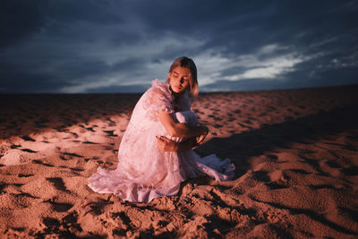 Woman sitting on sand in the evening illuminated by red light