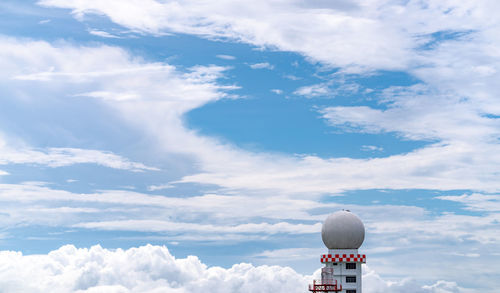 Weather observations radar dome station against blue sky and white fluffy clouds. 