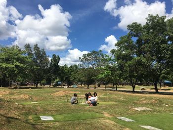 People sitting on field in park against sky