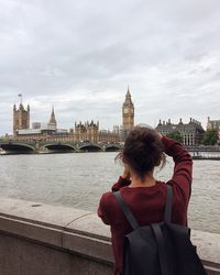 Rear view of woman standing by river with city in background