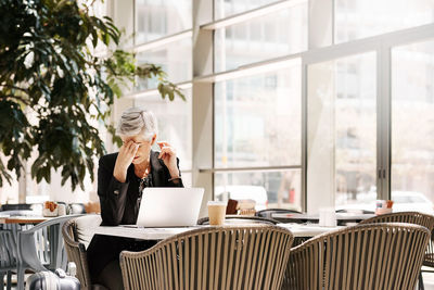 Young woman using phone while sitting on table