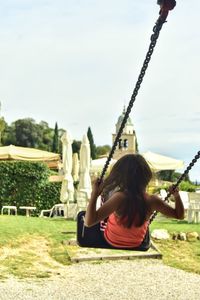 Rear view of young girl sitting on swing at playground