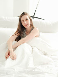 Portrait of young woman sitting on bed at home