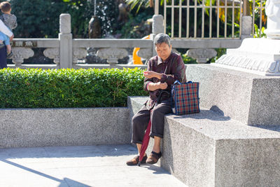 Full length of man using mobile phone while sitting on seat