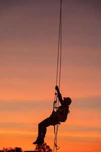 Silhouette man climbing on rope against sky during sunset