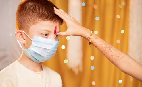 Cropped hand of sister applying tilaka to brother wearing mask at home