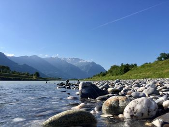 Rocks in lake against clear blue sky