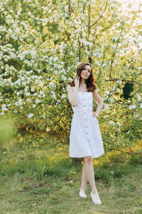 A cute happy young woman with a hairstyle in a white dress is walking enjoying nature in the summer