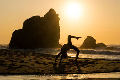 Silhouette of woman doing yoga on beach at sunset