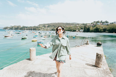 Portrait of young woman standing by lake against sky