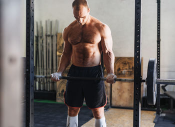 Shirtless muscular man lifting barbell while exercising in gym