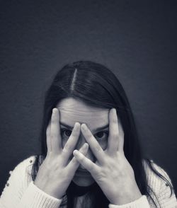 Portrait of beautiful young woman with hands covering eyes against wall