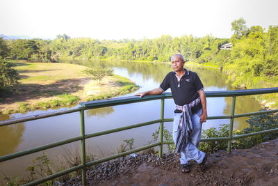 Portrait of man standing by railing against trees