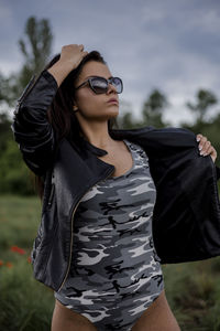 Sensuous young woman wearing camouflage bodysuit and leather jacket on field