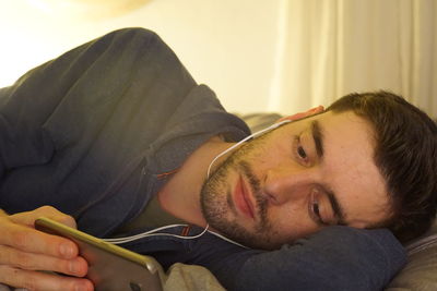 Close-up of man listening music while lying on bed at home