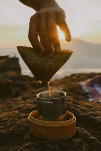 Close-up of hand holding coffee light against sky during sunrise