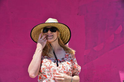 Woman wearing hat standing against pink wall