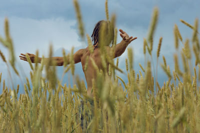 Shirtless man standing with arms outstretched on agricultural field against sky
