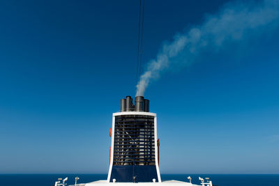 Smoke stack by sea against clear blue sky