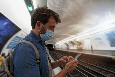 Side view of man wearing mask using phone at subway station