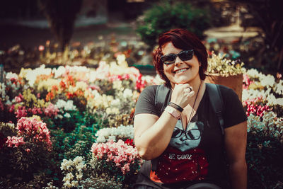 Portrait of smiling young woman with sunglasses against plants