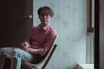 Young man looking away while sitting on chair at home