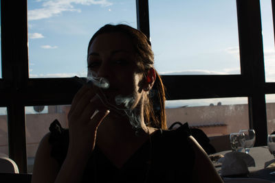 Woman smoking cigarette in restaurant against window