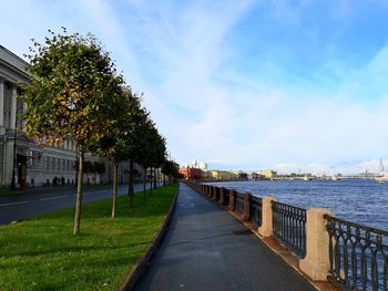 Footpath by river and buildings against sky