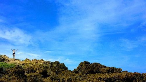 Woman on rocky mountain against blue sky