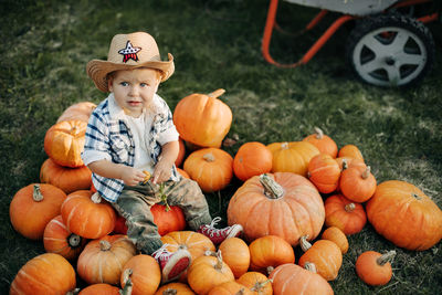 A charming baby in a cowboy hat is sitting on a large pile of pumpkins on the eve of halloween. 