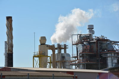 Low angle view of factory emitting smoke against blue sky