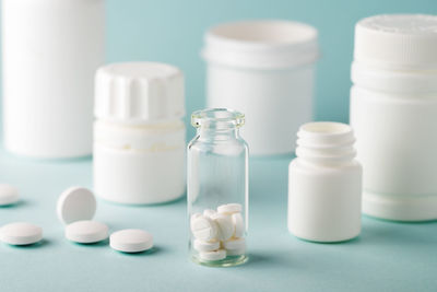 White pills in a small transparent jar on a blue background, copy space