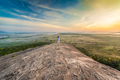 Rear view of man standing on rock against sky