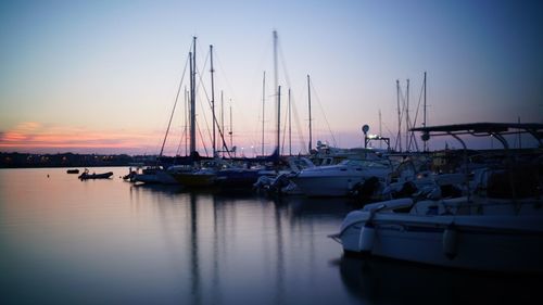 Sailboats moored on harbor against sky during sunset