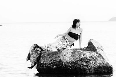 Woman sitting on rock by sea against sky