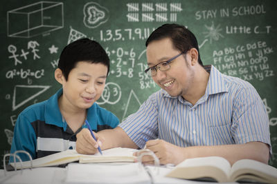 Boy with teacher at table against blackboard