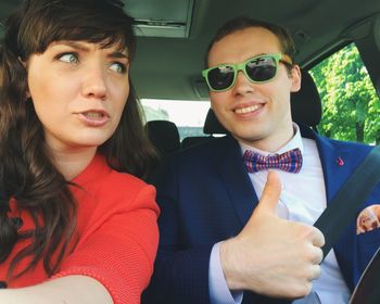 Smiling young man with woman showing thumbs up sign in car