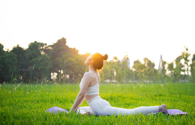 Rear view of woman doing yoga on field against clear sky